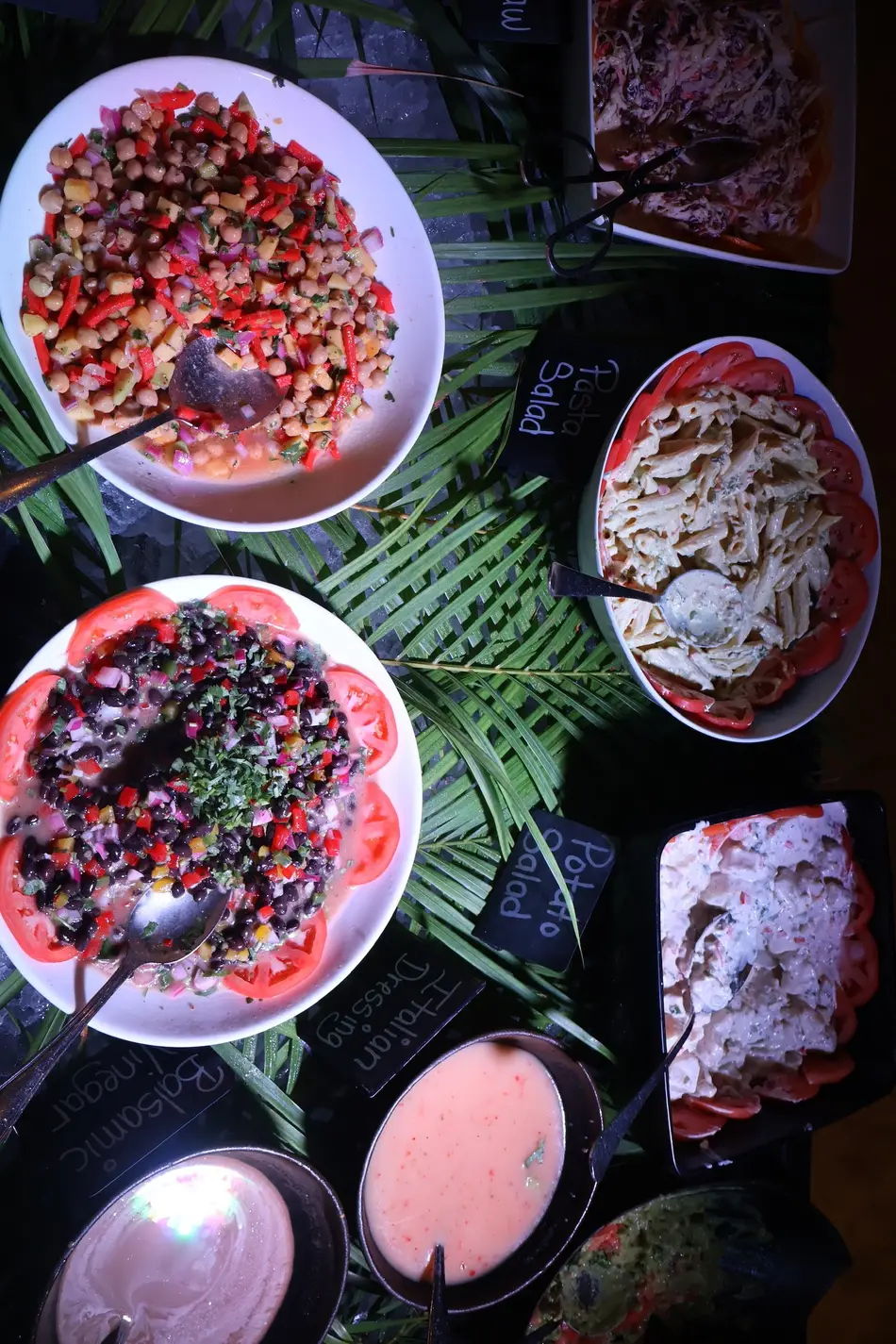 A spread of fresh salads — chickpea, black bean, pasta and potato — with dressings